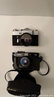 Front view of Zenit 8 SLR and Canon A35 F compact camera with case on white background.