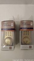 Two boxed Rona Collection electronic deadbolts with remote controls in brass finish shown side by side.
