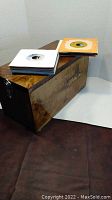 Custom wooden box with hinged lid and metal handles designed to store 45 RPM records, shown with some records stacked on top.