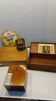 Photo showing the wooden Cuban humidor box, the Jean Valjean smoker's box open with the vintage cigar label inside, and the round Canadian Club metal sign.