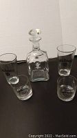 Set of one decanter and four Jack Daniel's branded glasses arranged on a dark surface against a white wall.