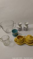 Photo showing all items in the lot including the clear glass mixing bowl, two white Lotte Norway candlestick holders with floral design, blue McCoy flower pot, yellow Fiesta creamer and sugar bowl on tray, and Heisey glass creamer