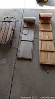 Three sledding items on concrete floor: from left, a wooden Streamliner sled with metal runners, aluminum toboggan in middle, and long wooden Mastercraft toboggan on right