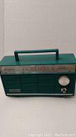 Front angled view of aqua blue Sony solid state transistor radio showing the tuning dial and speaker grill