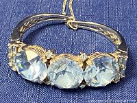 Close-up of front side showing three large oval baby blue rhinestones and smaller clear rhinestones on silver-gold tone expandable bracelet with safety chain.