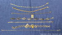 Top view of six silver bracelets and anklet arranged horizontally on blue fabric background.
