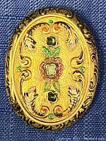 Photo of the pill box top showing gold tone with enamel detail and real stones on an oval silver base.