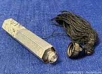 Photo showing the perfume bottle laying on blue fabric with black tassel and screw-on cap.