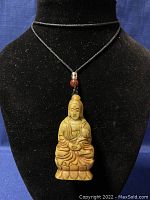 Full view of the carved jade pendant on a black cord displayed on a black stand.