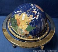 Globe made from blue lapis gemstone with continents represented by colored stones set within a gold-tone metal ring.