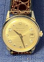 Front view of watch face showing champagne dial, diamond hour markers, date window at 3, gold tone case and crown, leather strap partially visible