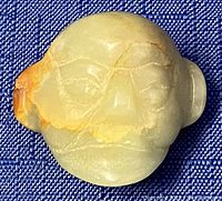 Front side of the carved green jade head pendant showing facial details and orange-brown discoloration.