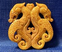 Close-up front view of the carved jade double-dragon amulet pendant on a blue fabric background showing details of dragon scales, tails, and central heart-shaped design.