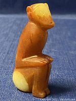 Front view of the carved jade sitting monkey pendant showing the figure's head, arms, legs, and the smooth surface with some color variation.