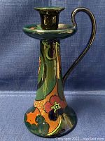 Front view of the decorative English pottery candleholder with floral patterns and curved handle.
