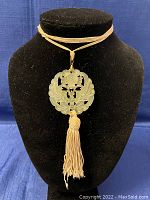Front view of the carved jade pendant on beige cord with tassel against black background.