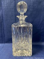 Full view of the clear crystal decanter with stopper on a dark blue background.