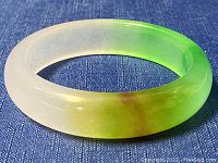 Side angle view of jade bangle showing color gradient from white to green and yellow with a brown spot
