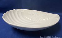 Side angled view of white ceramic clam-shaped serving dish showing ribbed texture and floral embossed details.