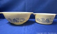 Two Pyrex Homestead cream-colored bowls with blue floral pattern on blue backdrop