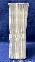 Front view of tall white bisque vase with vertical ridges and wavy top rim