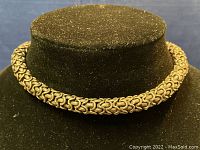 Front view of thick heavy silver necklace displayed on black stand, showing woven chain design.