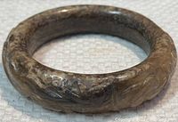 Close-up side view of carved jade bangle showing patina and surface details.