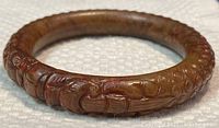Side angled view of the carved jade bangle showing textured floral and leaf patterns.