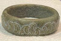 Close-up of the carved details on the jade bangle bracelet, showing the intricate symbols and floral patterns.