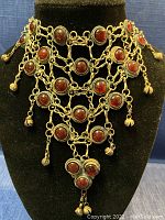 Front view of intricate old silver necklace featuring multiple round natural red stones and dangling silver bells, displayed on black velvet bust.