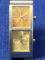 Close-up of the watch face showing two separate small square dials, one orange and one yellow, each with silver hands.