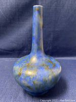 Front angle photo of the blue-brown speckled Tunstall Chameleon Ware vase with a long neck and rounded body.