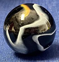 Top view of the black glass marble showing white and yellow swirl pattern.