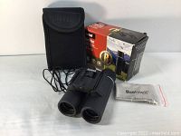 Image showing Bushnell binoculars, carry case, box, and lens cloth arranged on white surface
