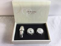 Opened gift box showing three skincare items with reflective silver packaging inside black foam insert.