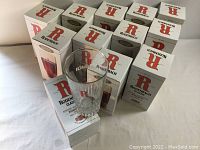 Photo showing 12 boxed Rodenbach Classic beer glasses arranged with one glass displayed out of its box, showing the red 'R' logo and faceted base.