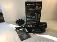 Photo showing black TRESemme hair dryer with folding handle, diffuser and box in the background
