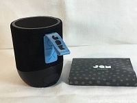 View of JAM Double Chill speaker showing fabric texture, black color, and blue carrying strap with JAM branding.
