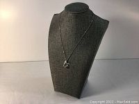 Silver necklace displayed on a dark grey bust stand, showing full length and pendant size.