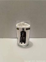 Clear cylindrical 8oz glass with printed black Batman figure and yellow black Batman logo, filled with white paper towel for display.