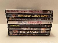 Stacked DVDs showing spine titles of 8 movies in action and thriller genres.