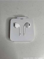 Pair of white Apple EarPods in original plastic packaging placed on a light-colored surface