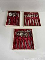 Photo showing three original boxes with cutlery items including forks, spoons, and serving spoons arranged on red satin lining.