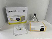 Photo showing LED multimedia projector, mini tripod, user manual, and product box with 1080p resolution mark.