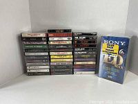 All cassette tapes stacked to show spines with album titles and artists, alongside sealed Sony VHS tape pack