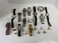 Photo showing 11 men's wristwatches in various styles including metal link and leather straps, and several pairs of cufflinks and pins arranged in front.