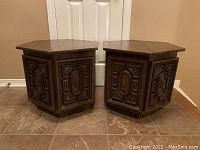 Pair of hexagonal wooden side tables with detailed carved front panels and dark wood finish placed on tiled floor.