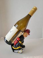 The firefighter holding a wine bottle on his back, shown from a side angle to display the bottle placement and figure details.