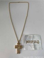 Photo of gold-tone cross pendant necklace with packaging paper titled Inch Of Gold.