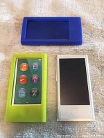 Two silicone cases (blue and green) shown alongside Apple iPod Nano Gen 7 model A1446 silver device on fabric surface.